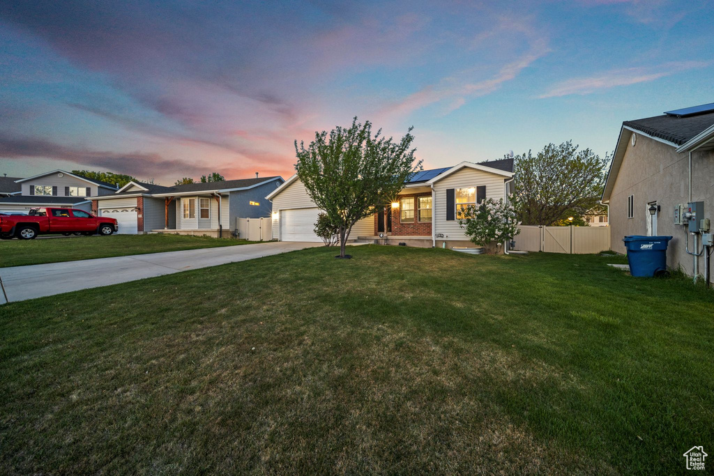 Ranch-style home with a lawn, fence, driveway, and solar panels
