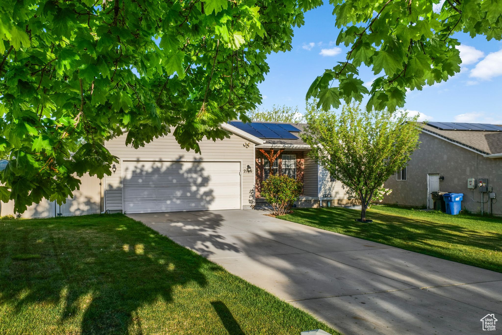 View of front of house featuring a garage, driveway, a front yard, and solar panels