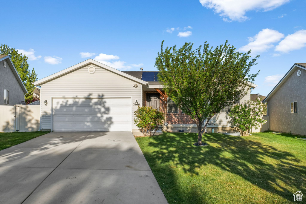 Ranch-style house with driveway, solar panels, a front yard, brick siding, and an attached garage