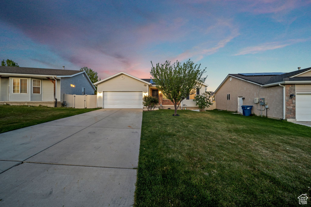 Ranch-style home with concrete driveway, fence, roof mounted solar panels, and a front lawn