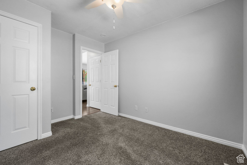 Unfurnished bedroom featuring dark colored carpet, baseboards, and ceiling fan