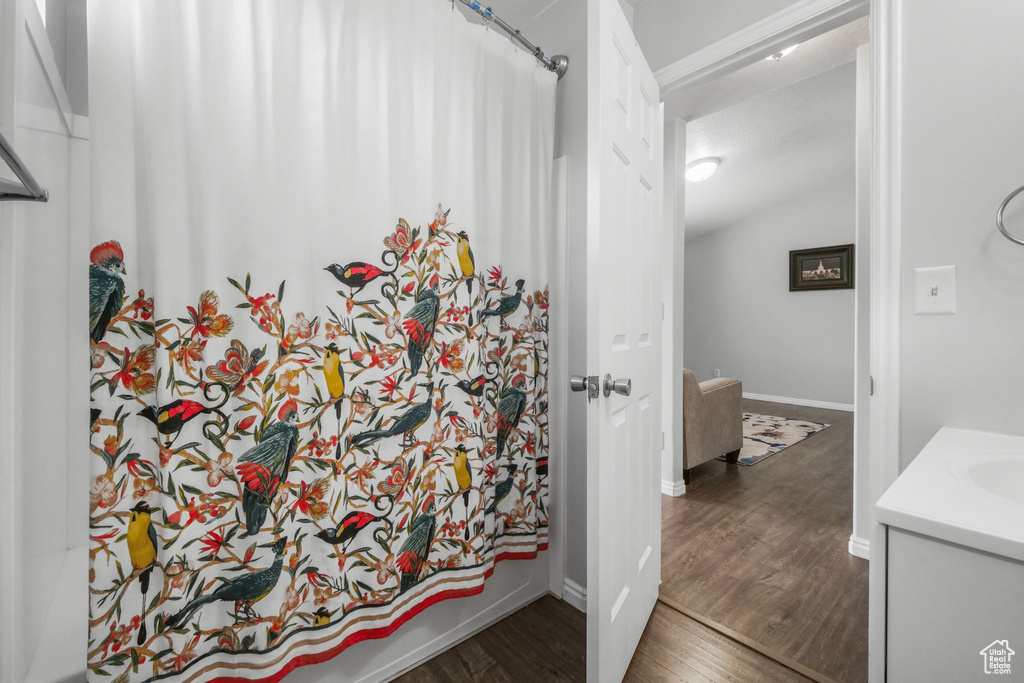 Full bathroom featuring vanity, a shower with shower curtain, baseboards, wood finished floors, and lofted ceiling