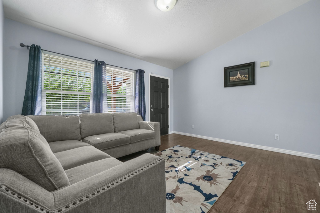 Living room with dark wood-type flooring, baseboards, and vaulted ceiling