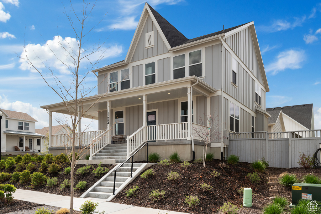 Farmhouse-style home featuring fence, covered porch, board and batten siding, and stairway