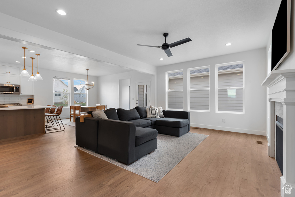 Living room featuring light wood finished floors, a fireplace, ceiling fan with notable chandelier, recessed lighting, and baseboards