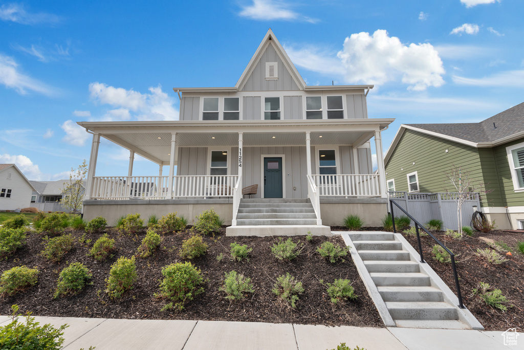 View of front of property with a porch, board and batten siding, fence, and stairway