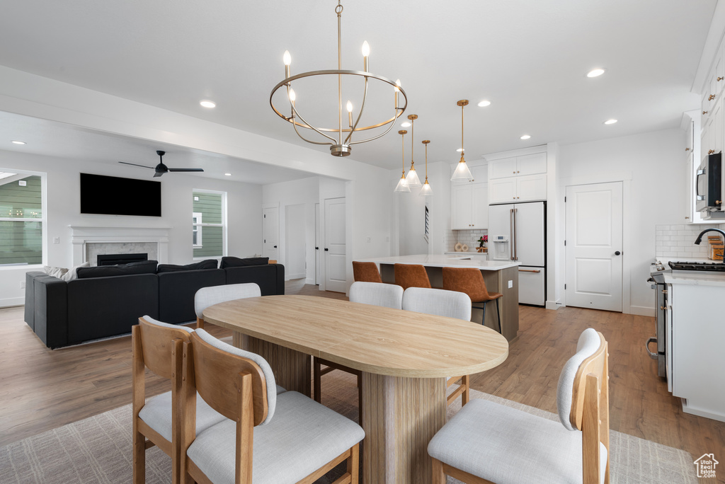 Dining area featuring light wood-type flooring, recessed lighting, ceiling fan with notable chandelier, and a fireplace