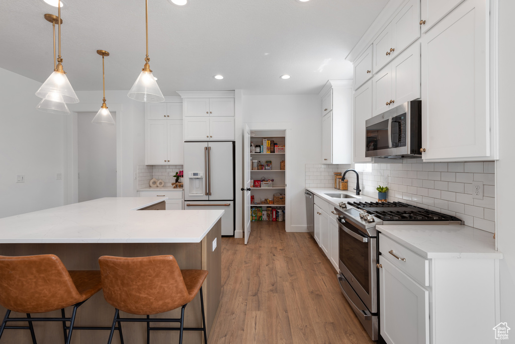 Kitchen with a kitchen island, tasteful backsplash, a sink, light wood finished floors, and appliances with stainless steel finishes