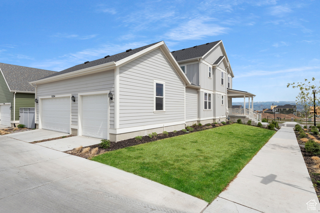 View of property exterior featuring a yard, a porch, driveway, board and batten siding, and an attached garage