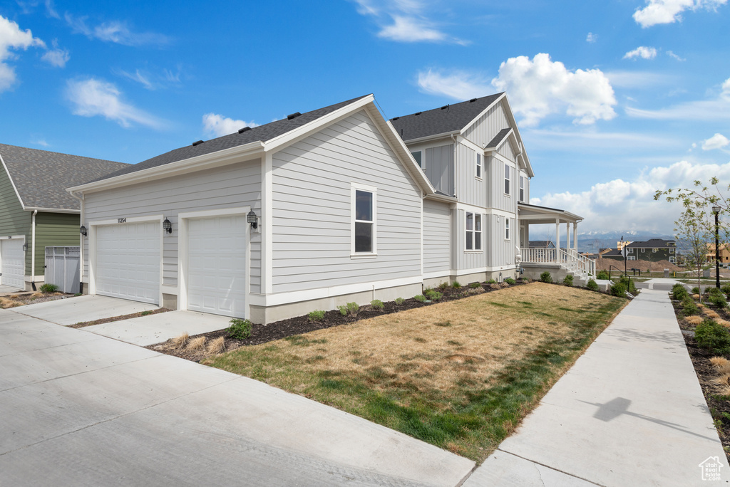 View of side of property with a garage, a lawn, board and batten siding, concrete driveway, and a porch