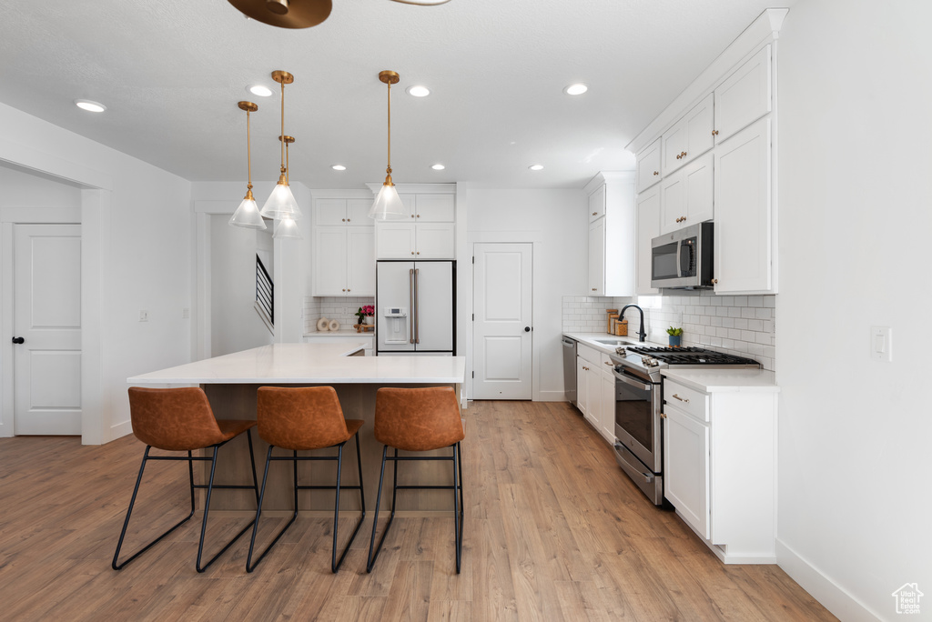 Kitchen featuring a kitchen bar, appliances with stainless steel finishes, tasteful backsplash, a sink, and white cabinets