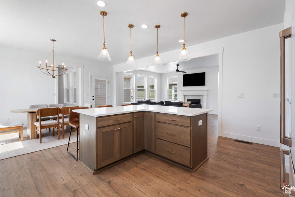 Kitchen with visible vents, a fireplace, dark wood finished floors, light countertops, and ceiling fan with notable chandelier