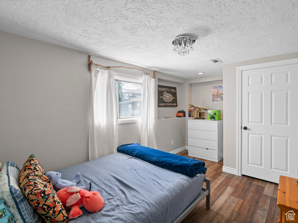 Bedroom with a textured ceiling, baseboards, hardwood / wood-style floors, and visible vents