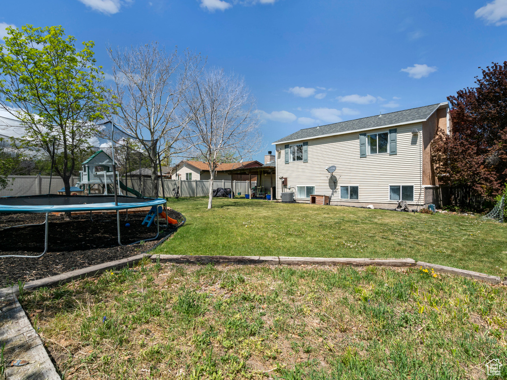 Rear view of house featuring a fenced backyard, a trampoline, and a yard