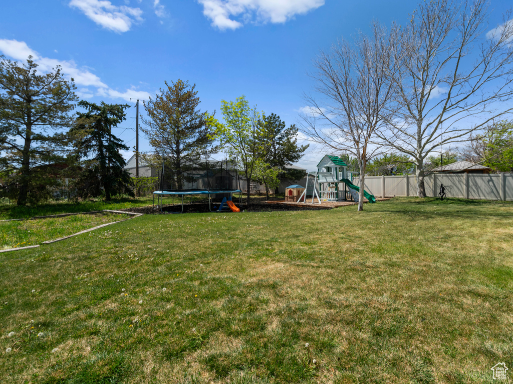 View of yard featuring a playground, fence, and a trampoline