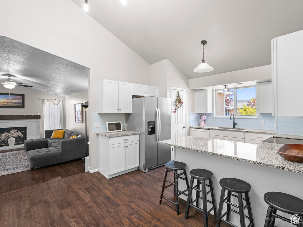 Kitchen with white cabinets, a sink, stainless steel fridge with ice dispenser, a breakfast bar area, and lofted ceiling