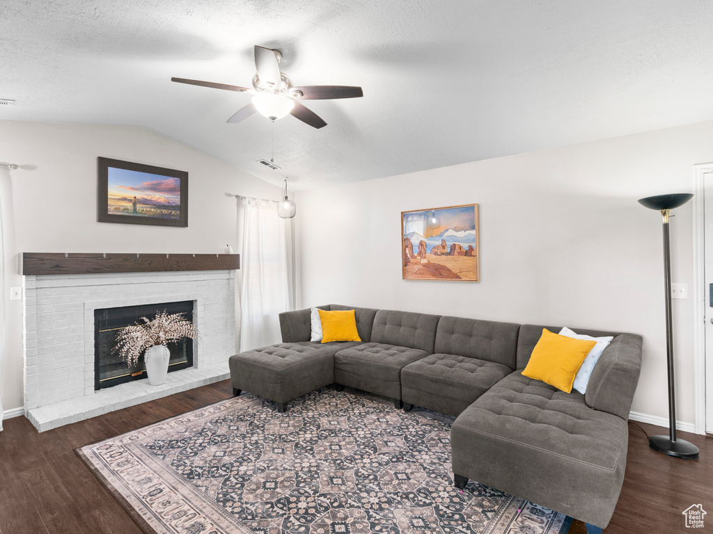 Living room featuring ceiling fan, a brick fireplace, baseboards, wood finished floors, and lofted ceiling
