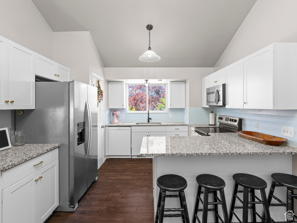 Kitchen with white cabinetry, a peninsula, vaulted ceiling, and stainless steel appliances