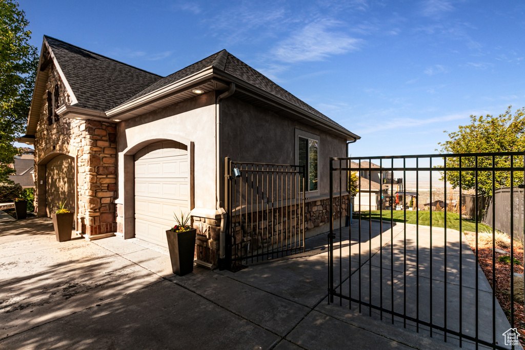 View of home\\\'s exterior featuring roof with shingles, fence, an attached garage, and stone siding