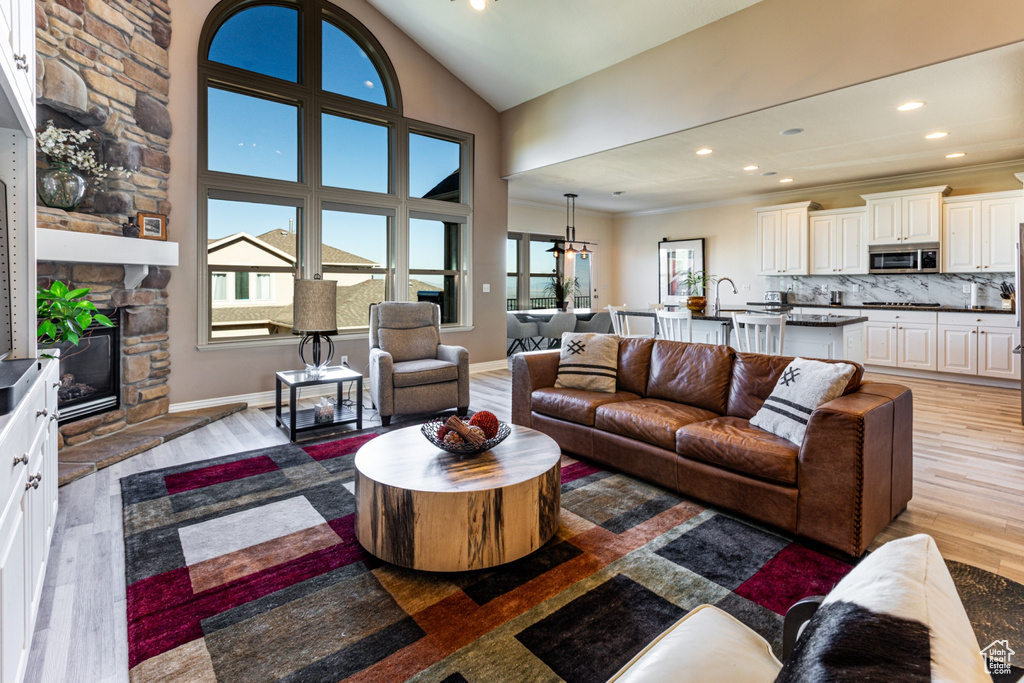 Living area featuring a stone fireplace, light wood-type flooring, lofted ceiling, ornamental molding, and recessed lighting