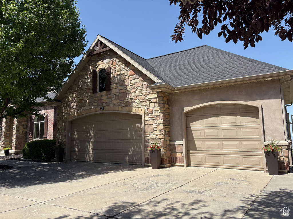 View of front of home featuring a shingled roof, stone siding, a garage, stucco siding, and concrete driveway