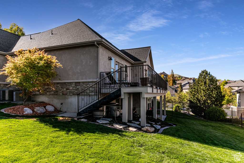 Rear view of property with fence, a shingled roof, stucco siding, stairway, and a lawn