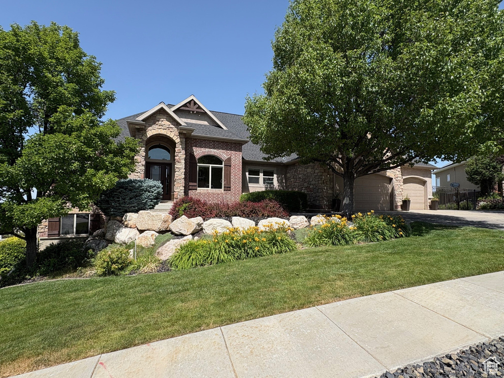 View of front facade with driveway, stone siding, a front lawn, brick siding, and a garage
