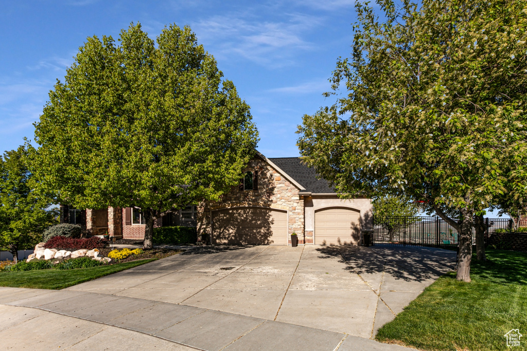 View of property hidden behind natural elements with fence, stone siding, a garage, stucco siding, and driveway
