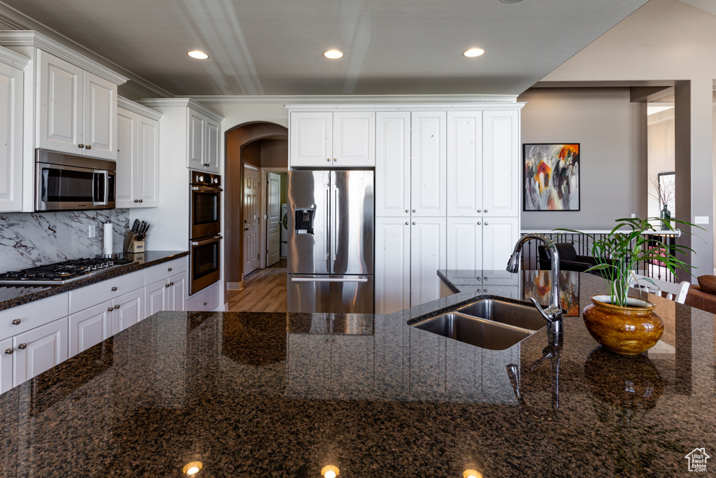 Kitchen with arched walkways, tasteful backsplash, a sink, white cabinets, and stainless steel appliances
