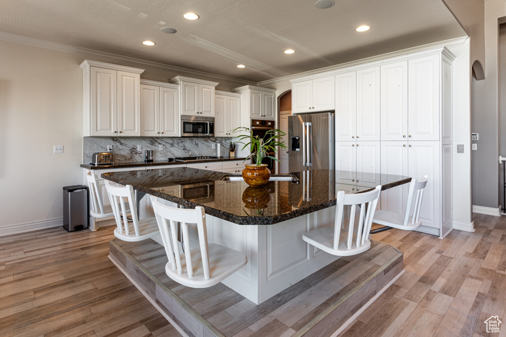 Kitchen featuring decorative backsplash, baseboards, a kitchen bar, arched walkways, and stainless steel appliances
