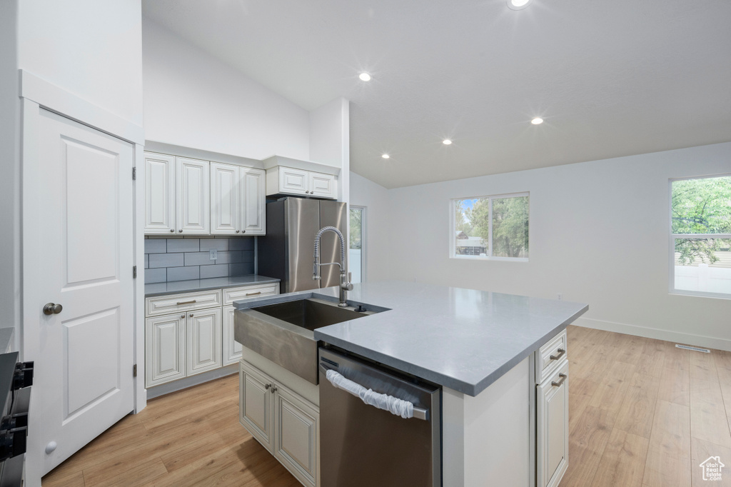 Kitchen with a kitchen island with sink, tasteful backsplash, a sink, light wood-style flooring, and stainless steel appliances