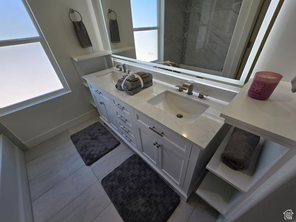 Bathroom featuring double vanity, baseboards, tile patterned floors, and a tile shower
