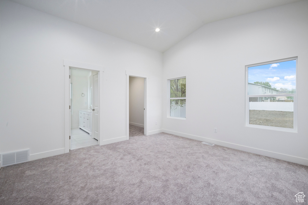 Unfurnished bedroom featuring visible vents, baseboards, a walk in closet, high vaulted ceiling, and light colored carpet
