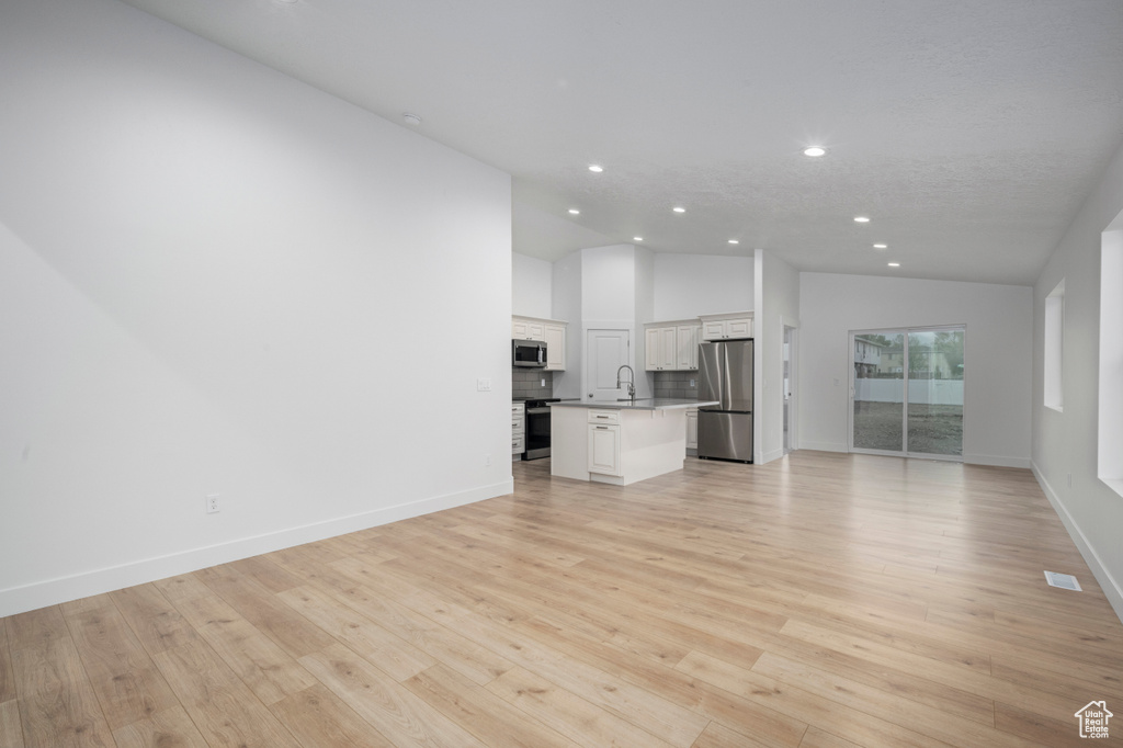 Unfurnished living room featuring a sink, baseboards, light wood-type flooring, and recessed lighting