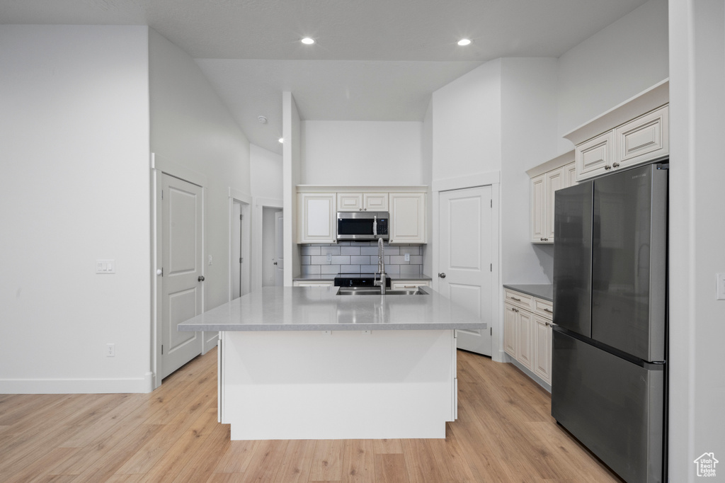 Kitchen featuring light wood-style floors, appliances with stainless steel finishes, tasteful backsplash, and a towering ceiling