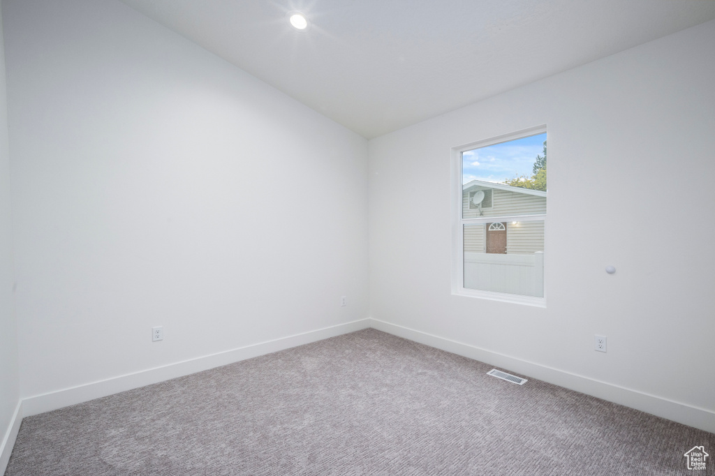Carpeted empty room with baseboards, vaulted ceiling, and visible vents