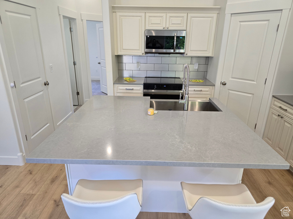 Kitchen with stainless steel microwave, a sink, light wood-style floors, decorative backsplash, and a center island with sink