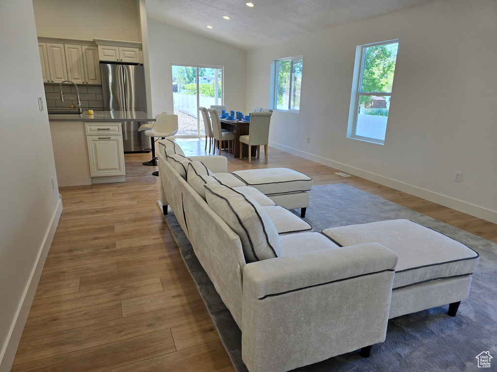 Living room featuring vaulted ceiling, baseboards, light wood-style floors, and recessed lighting