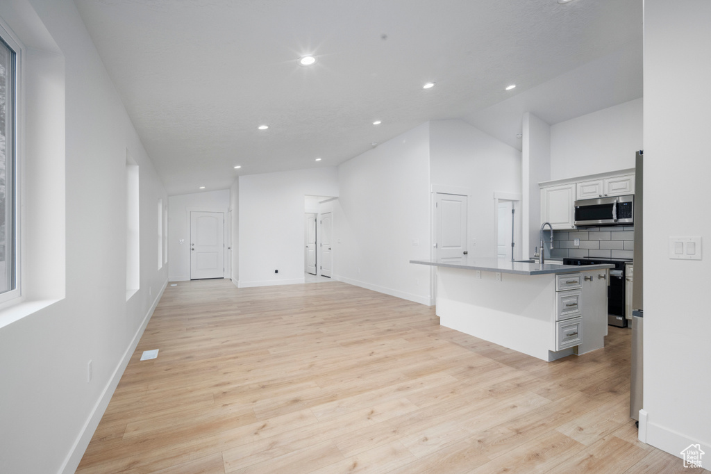 Kitchen featuring light wood finished floors, recessed lighting, stainless steel microwave, tasteful backsplash, and vaulted ceiling
