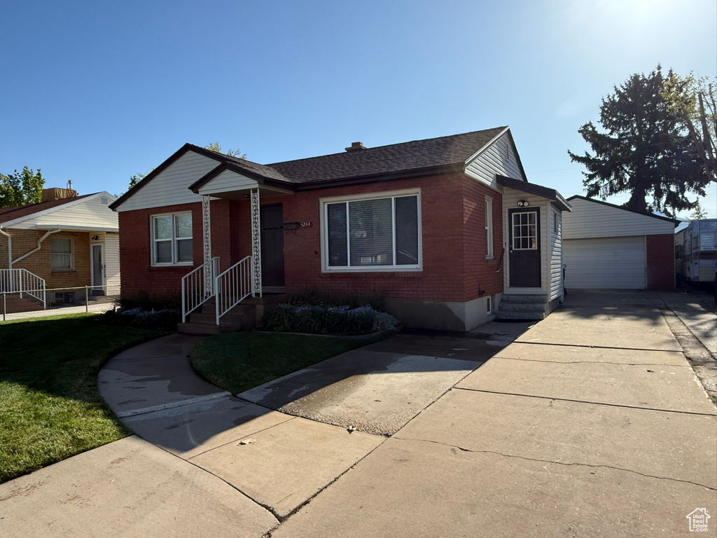 View of front facade featuring brick siding, a garage, a front lawn, and an outbuilding