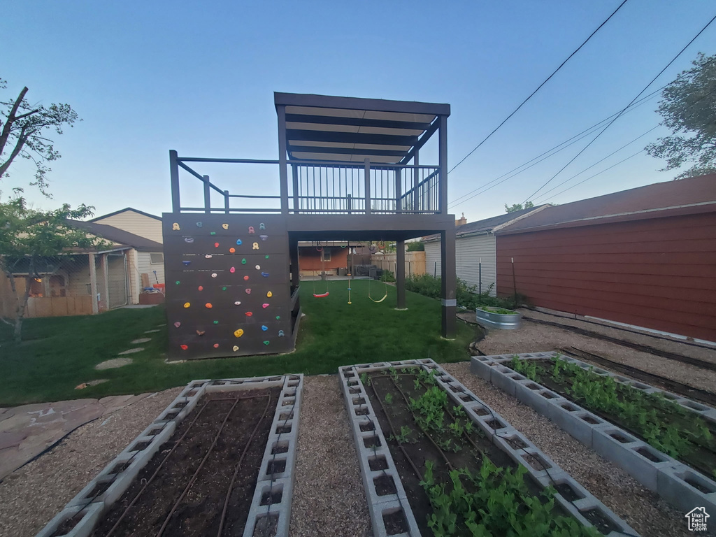 Back of house featuring a wooden deck, fence, a vegetable garden, a playground, and a lawn