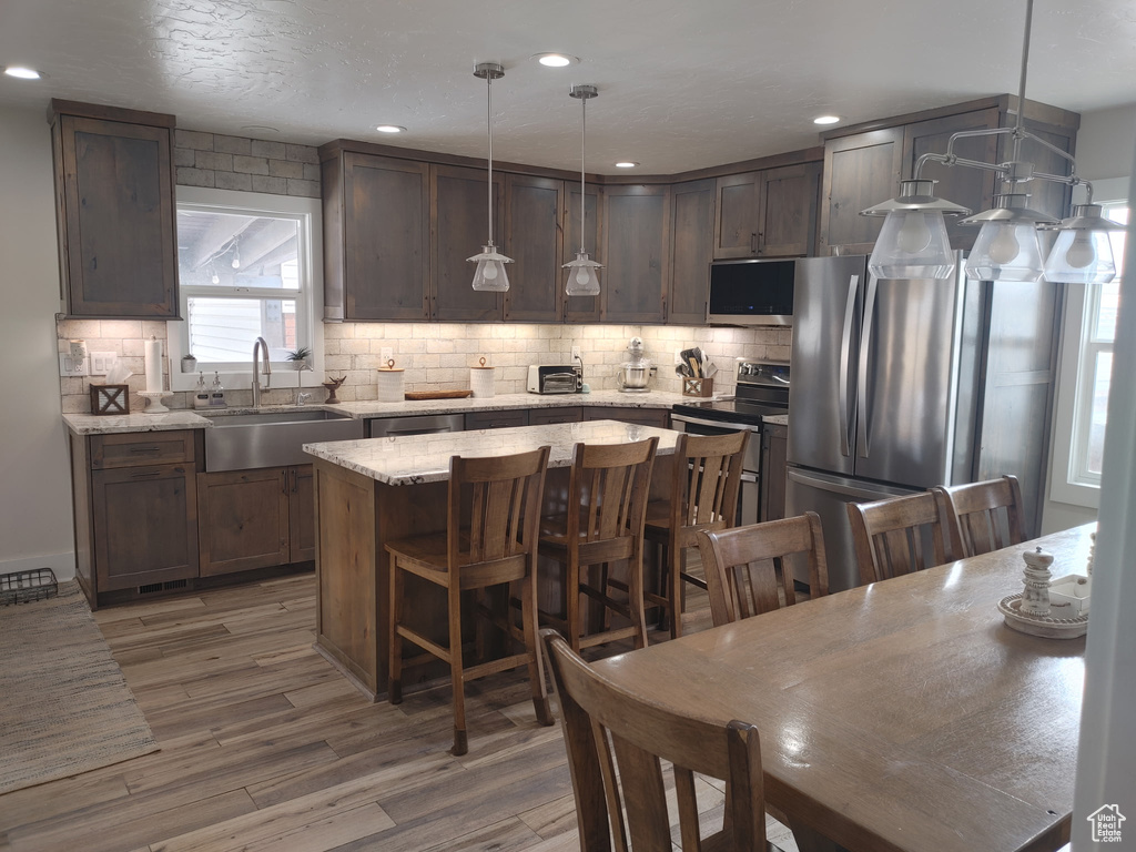 Kitchen featuring light wood-style floors, appliances with stainless steel finishes, a sink, and tasteful backsplash