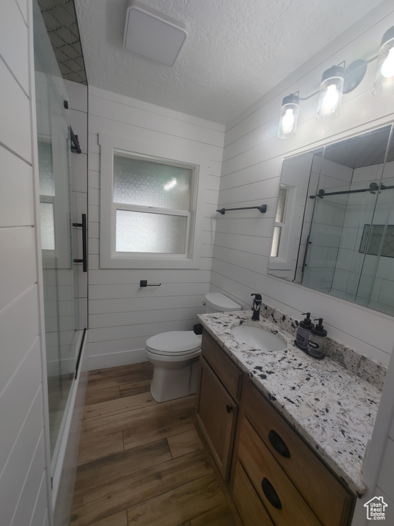 Bathroom with toilet, a textured ceiling, wood finished floors, and a stall shower