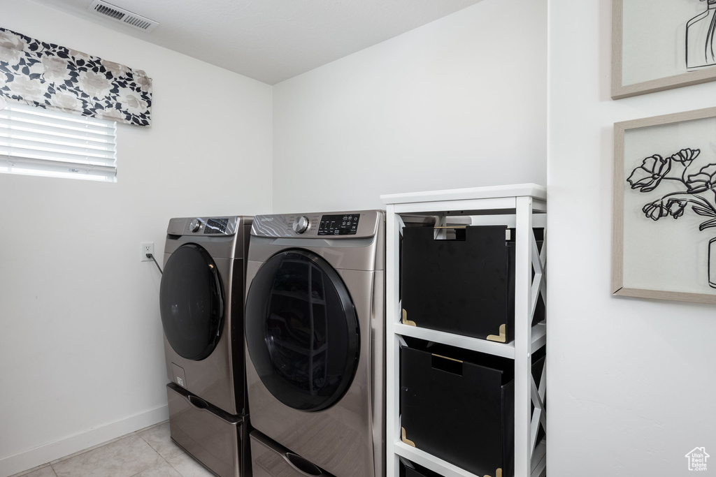 Clothes washing area with laundry area, washing machine and clothes dryer, visible vents, light tile patterned floors, and baseboards
