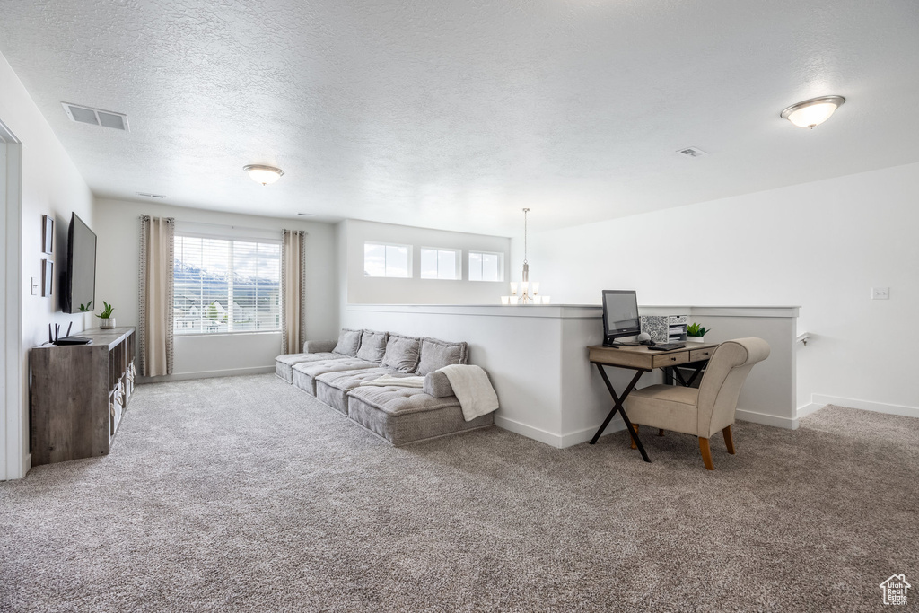 Living area with a textured ceiling, visible vents, carpet floors, baseboards, and a chandelier