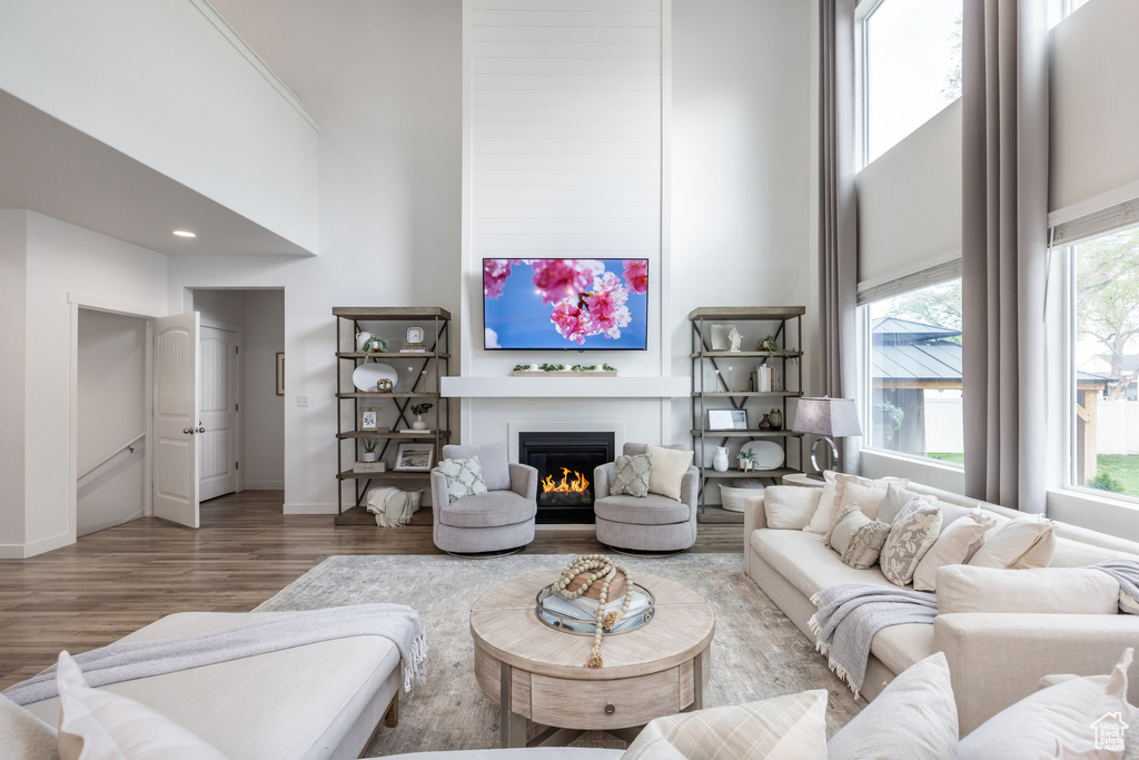 Living room with baseboards, a lit fireplace, wood finished floors, and a towering ceiling