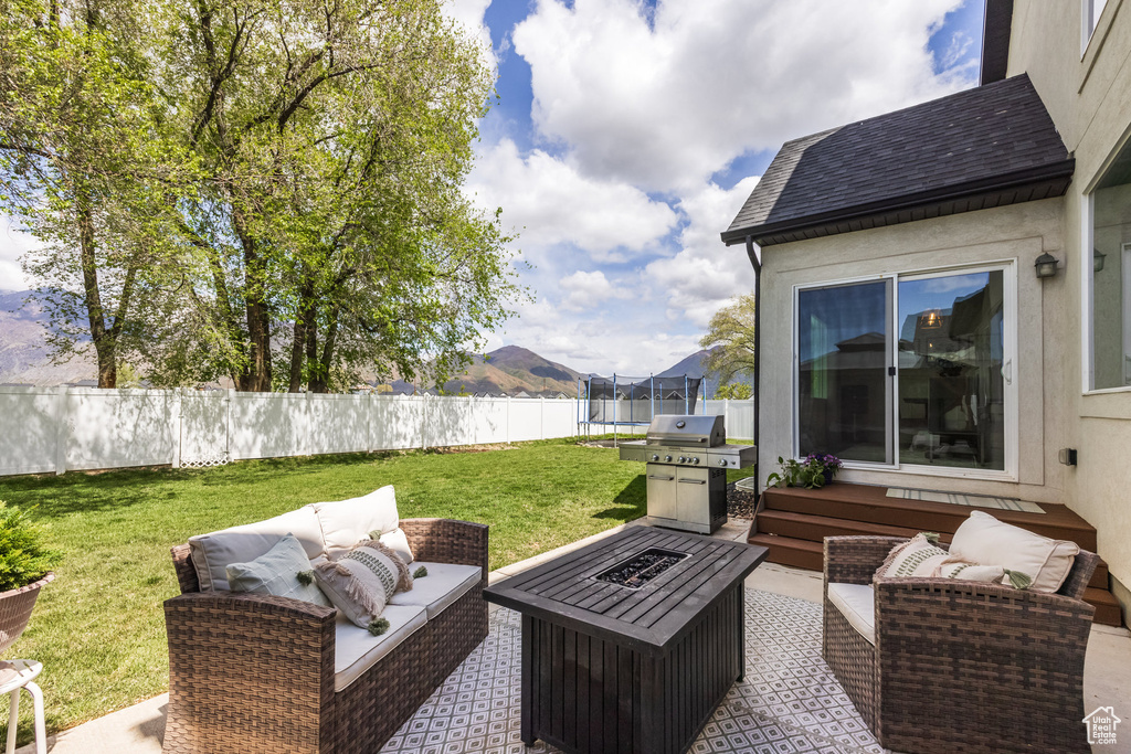 View of patio with fence, a mountain view, a trampoline, and an outdoor living space with a fire pit