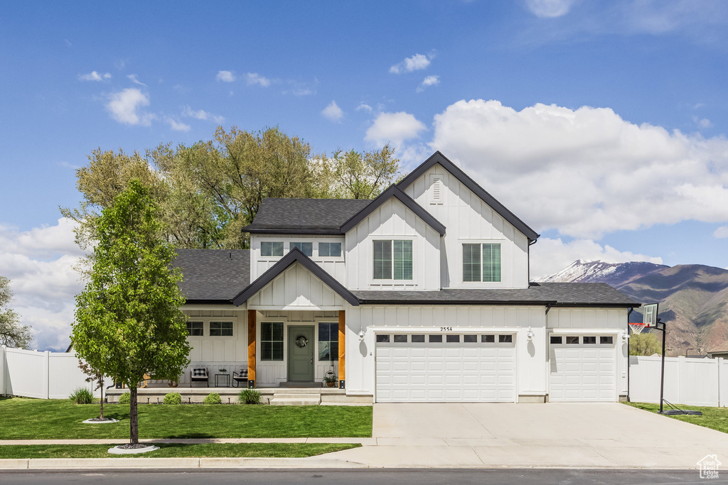 View of front of home featuring fence, roof with shingles, a front lawn, board and batten siding, and driveway