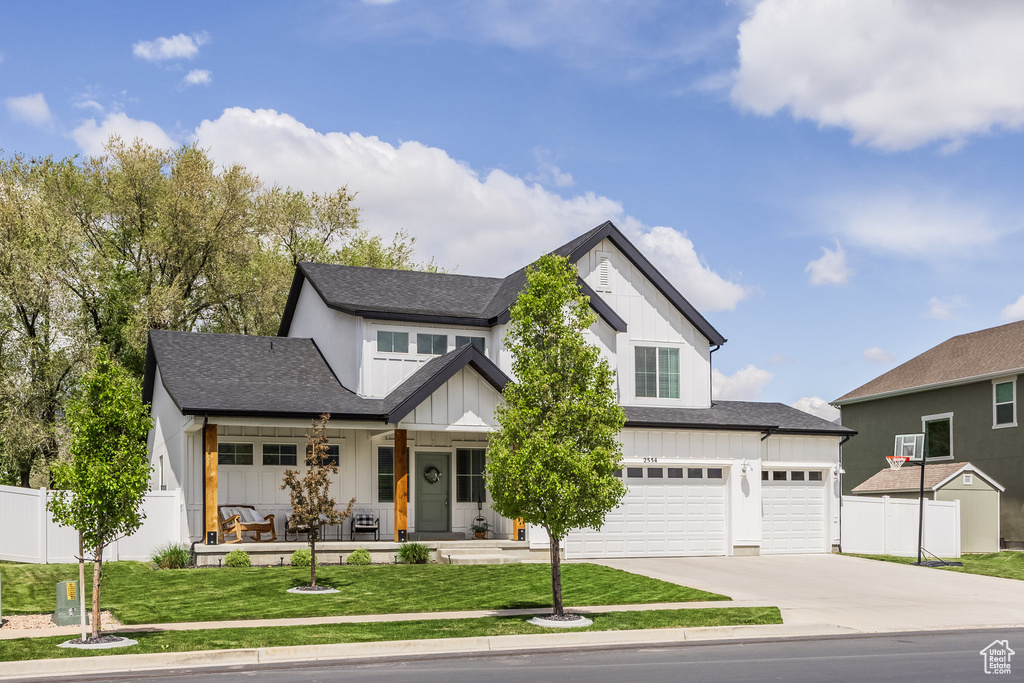 Modern farmhouse style home featuring fence, a front yard, board and batten siding, a porch, and driveway