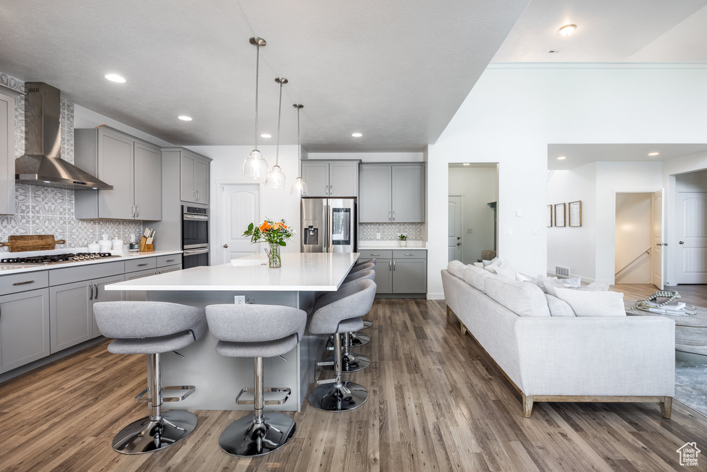 Kitchen with gray cabinetry, stainless steel appliances, wall chimney range hood, and a kitchen bar